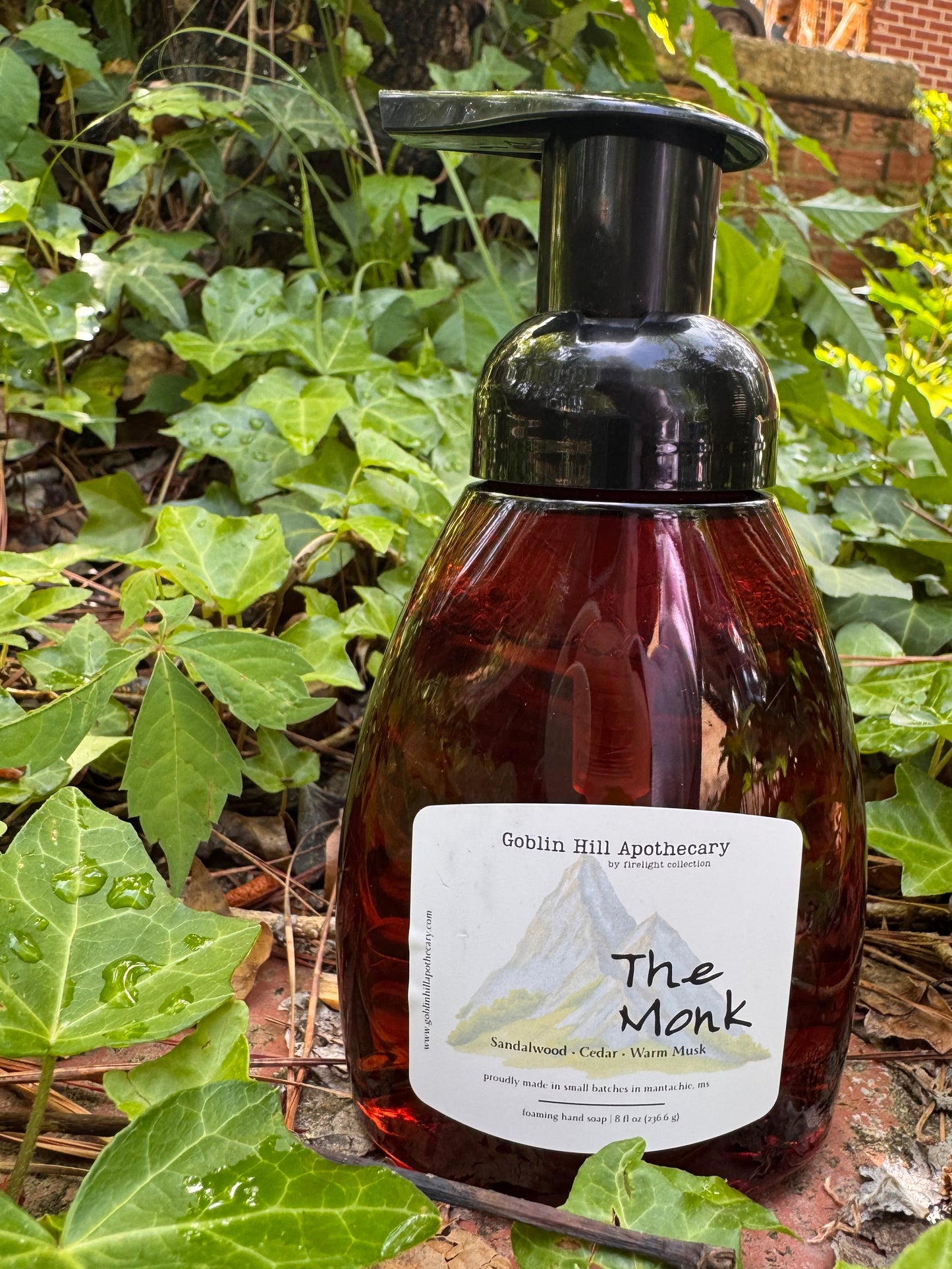 Bottle of 'The Monk' hand soap with a label on a tree branch surrounded by green leaves.