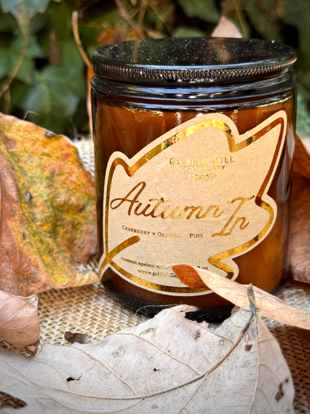 an amber candle jar surrounded by leaves