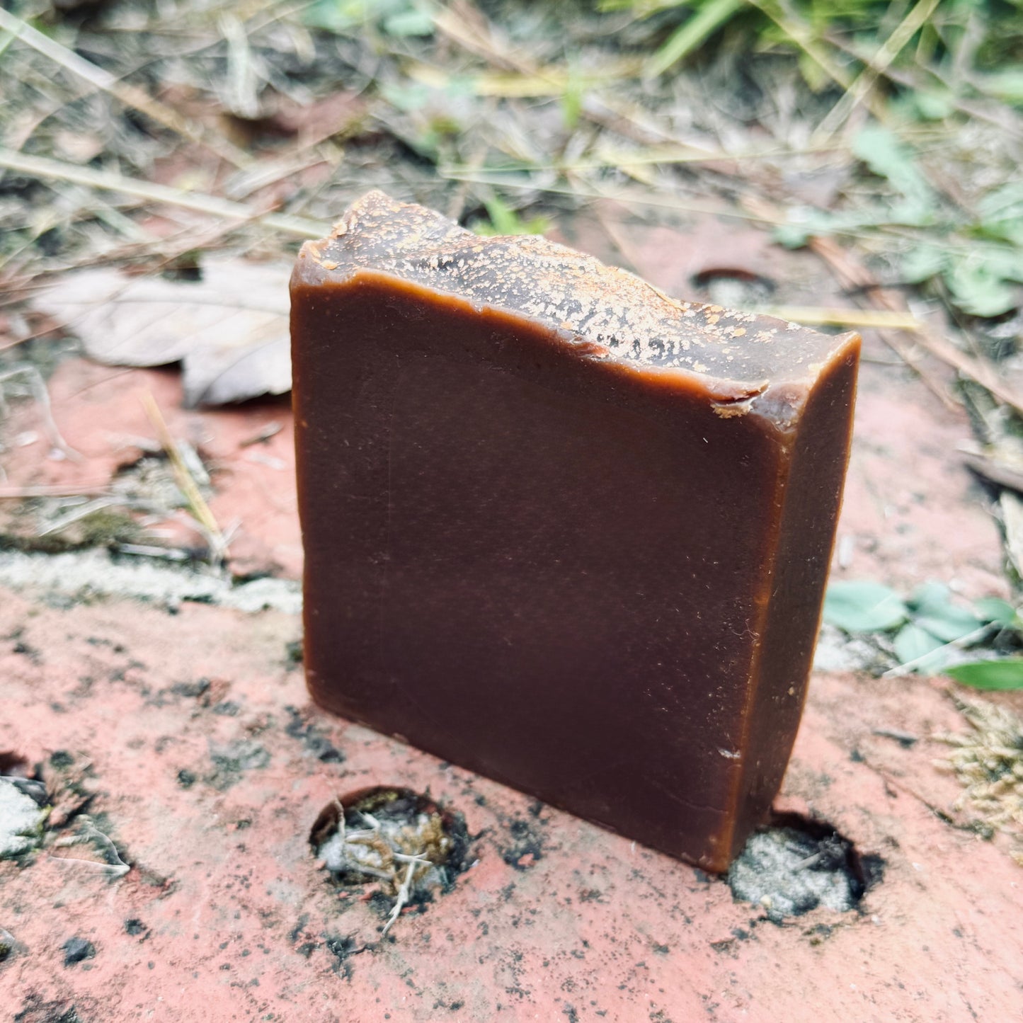 Brown bar of soap on a textured surface with grass in the background