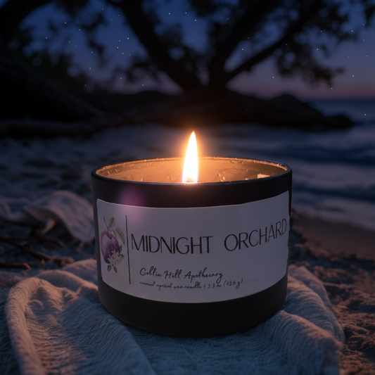 Candle labeled 'Midnight Orchard' on a beach at sunset