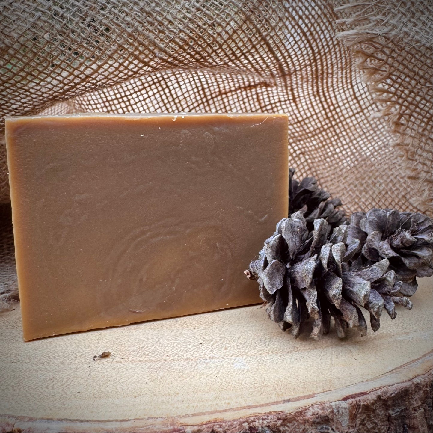 Bar of soap next to a pine cone on a wooden surface with burlap in the background