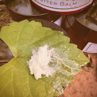 White substance on a green leaf with a jar labeled 'Butter Balm' in the background.