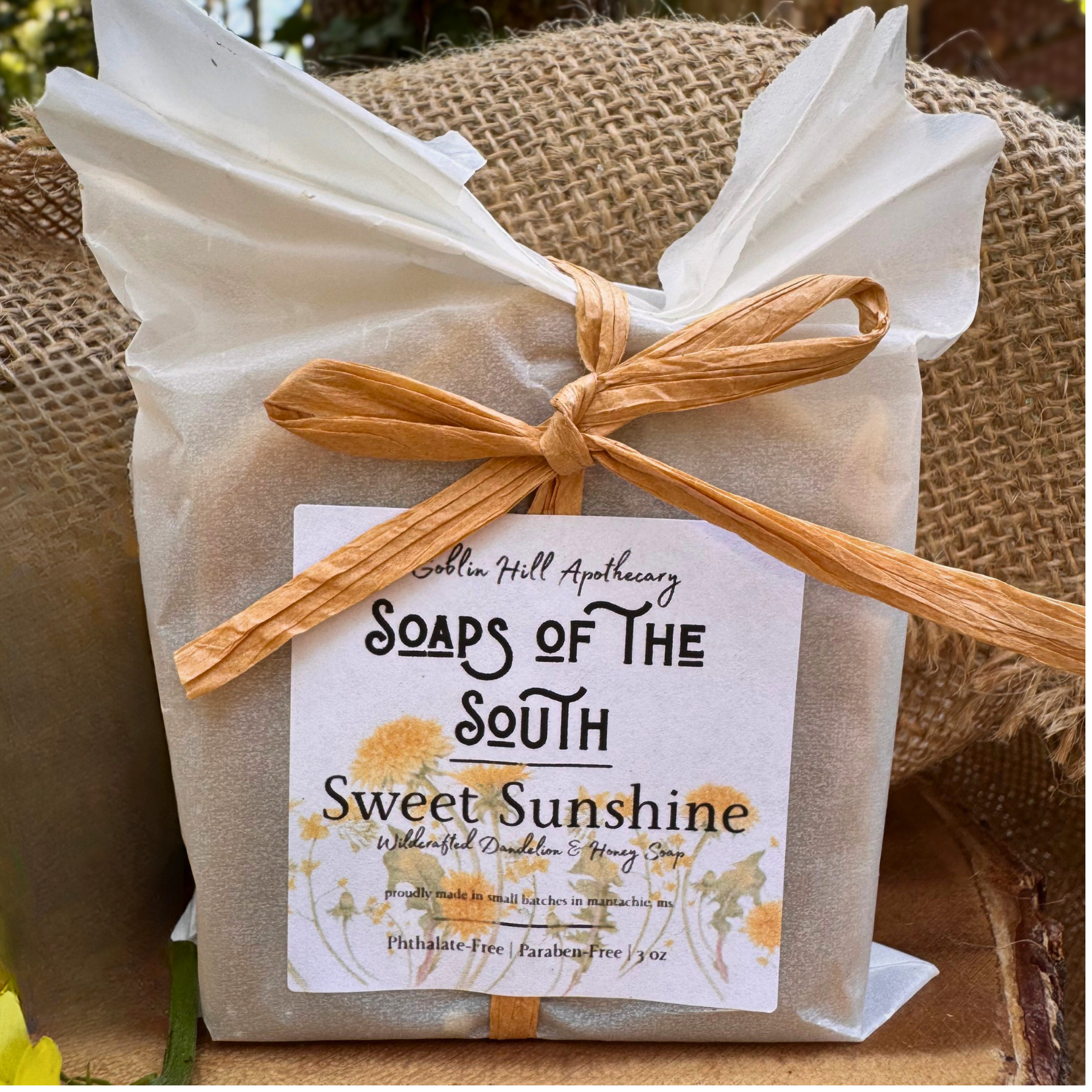 Product packaging of 'Soaps of the South Sweet Sunshine' with a label and decorative bow on a natural background.