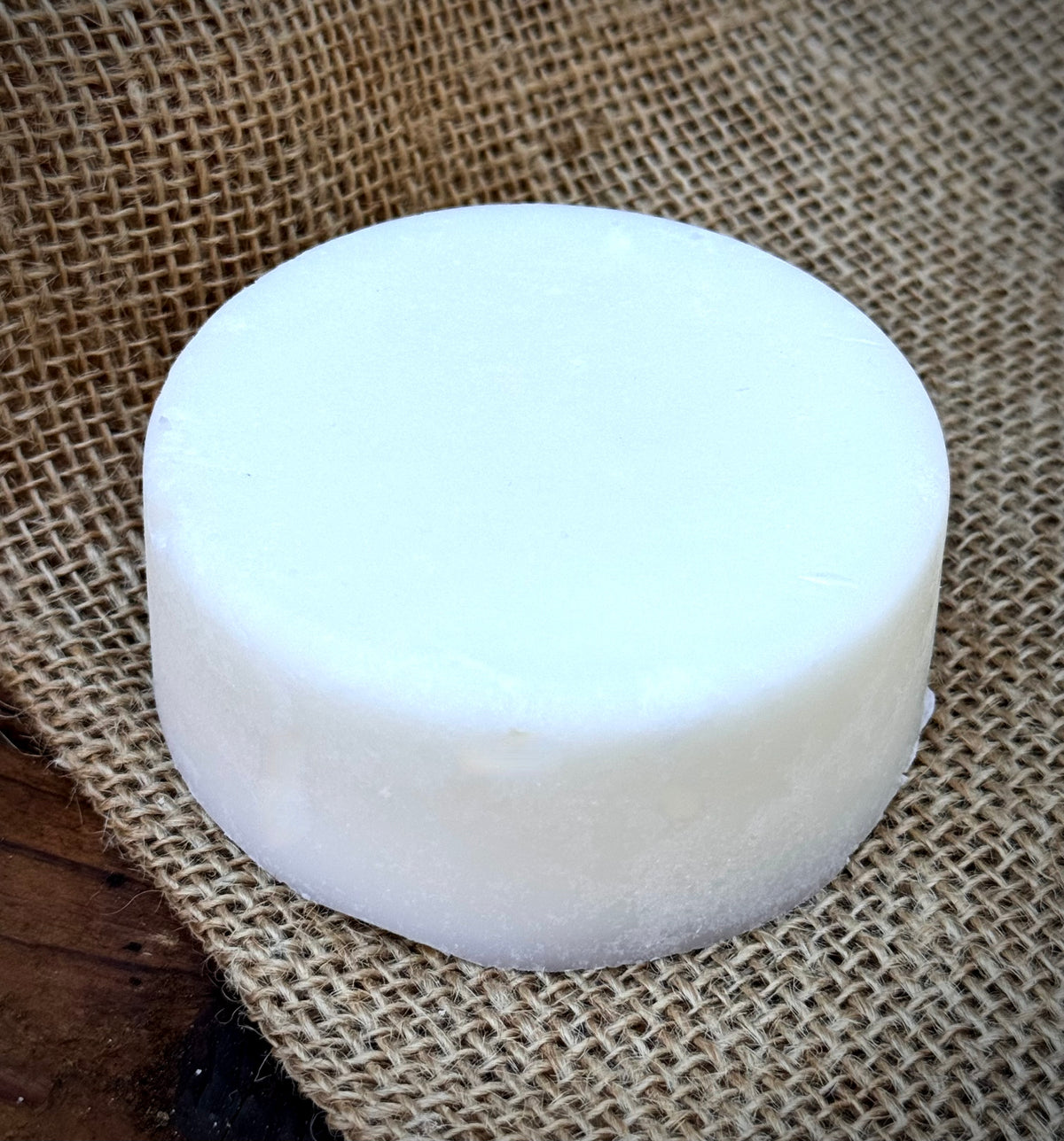 A round white bar of soap  resting on a textured burlap fabric background.