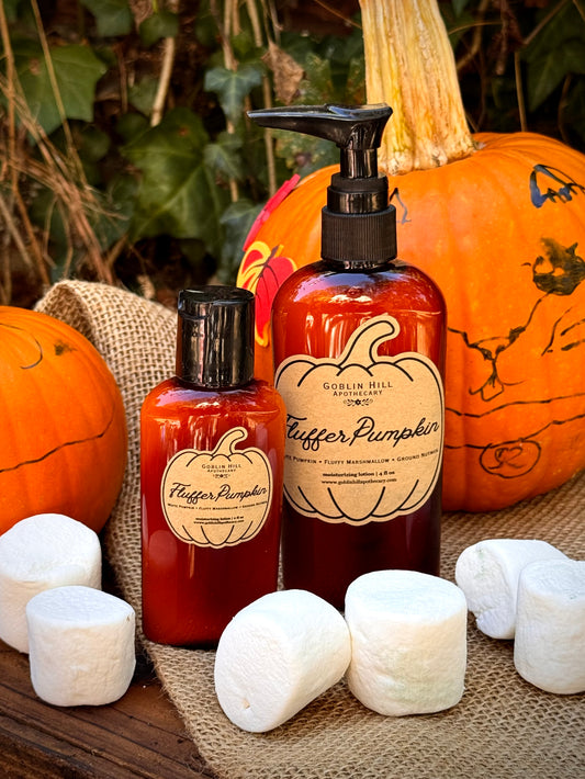 Two amber pump and cap bottles labeled 'Coconut Hill Apothecary Co.' 'Hunger Pumpkin' arranged on burlap with whole pumpkins and white marshmallows in a fall-themed setting.