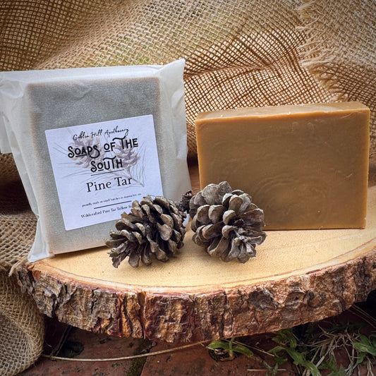 Two bars of soap with a label, two pine cones on a wooden surface with burlap in the background.