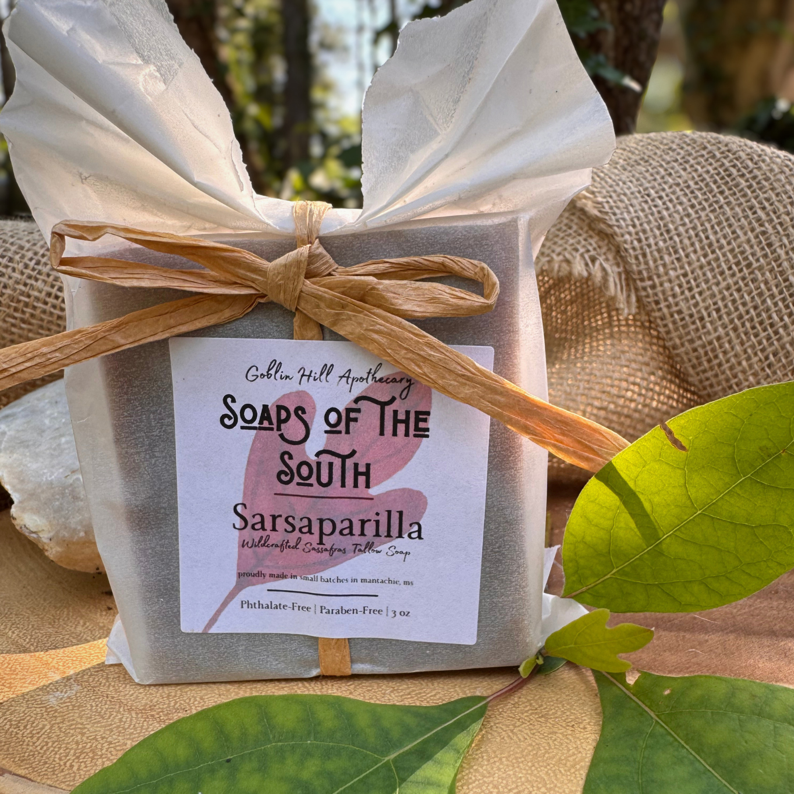 Bar of soap wrapped in white paper with a bow, labeled 'Soaps of the South Sarsaparilla', on a natural background.