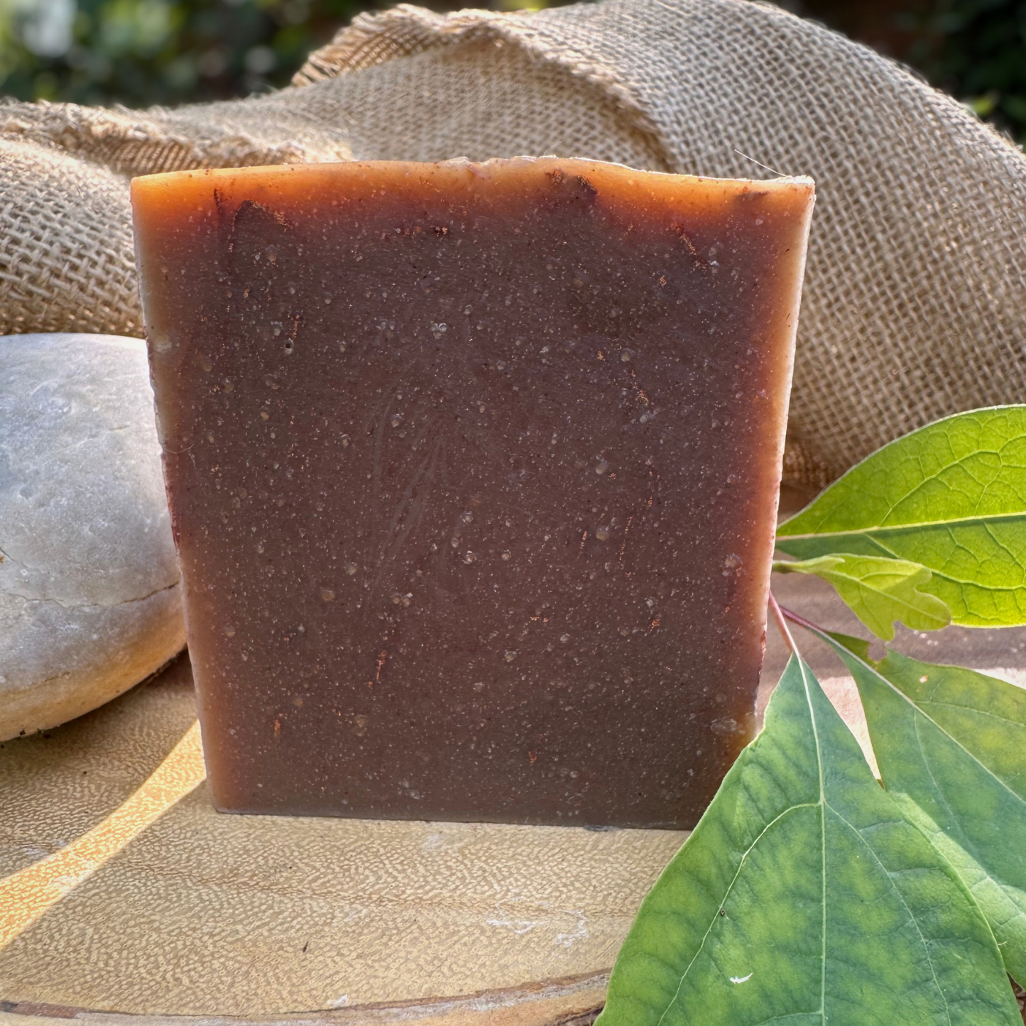 Brown bar of soap on a stone surface with green leaves and burlap in the background